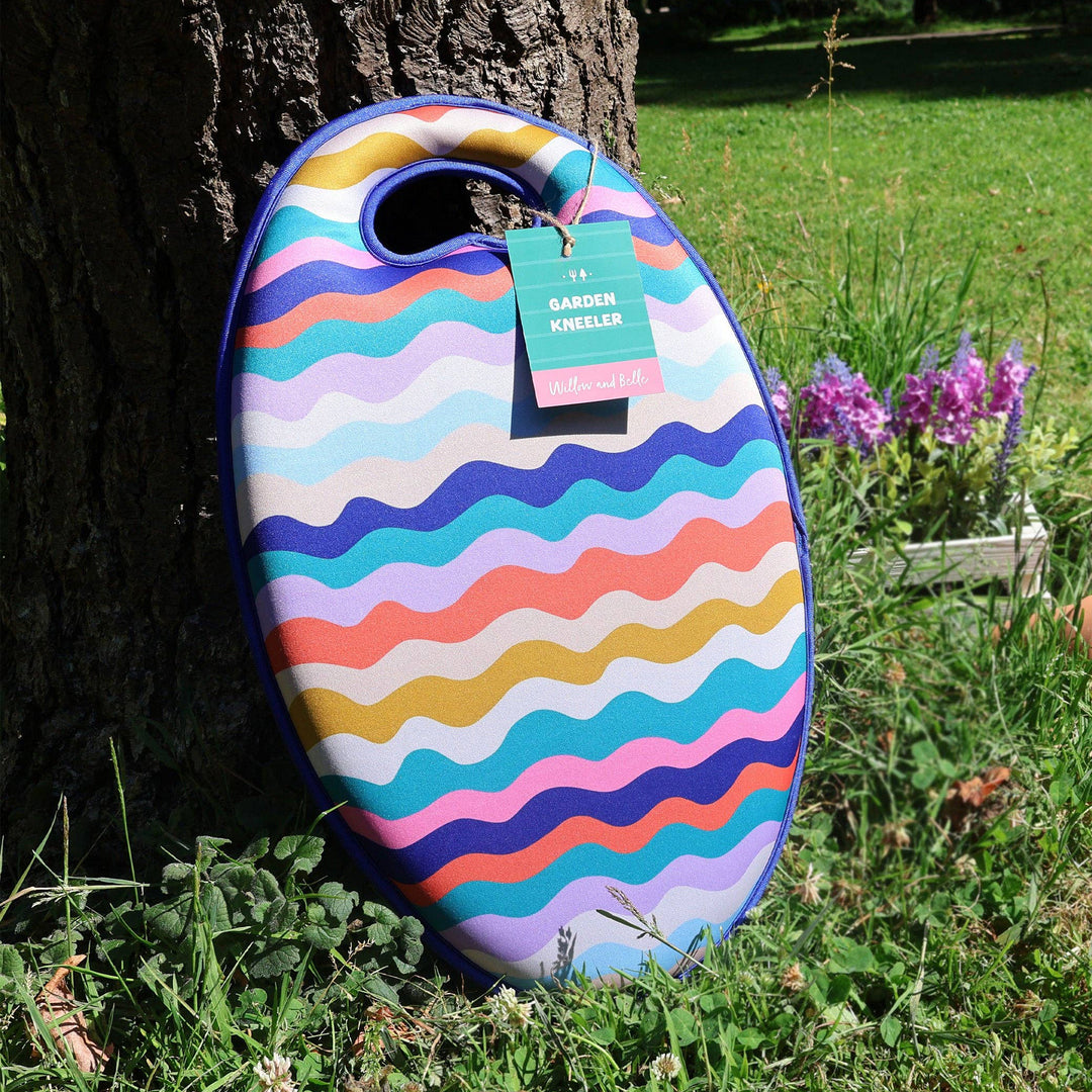 Colorful wavy-patterned garden kneeler leaning against a tree with flowers in the background.