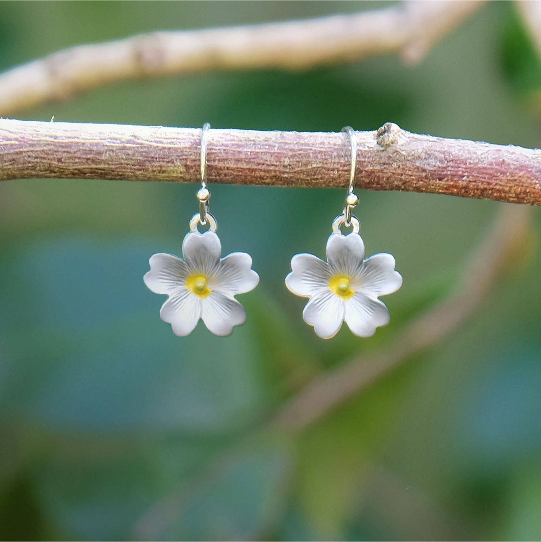 Flower-shaped earrings hanging on a branch with a natural background