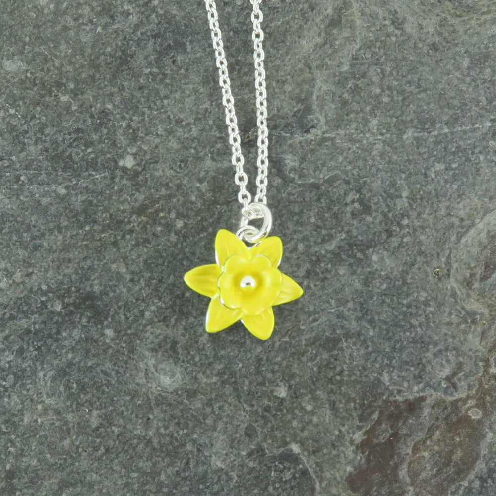 Yellow flower pendant on a silver chain against a gray stone background