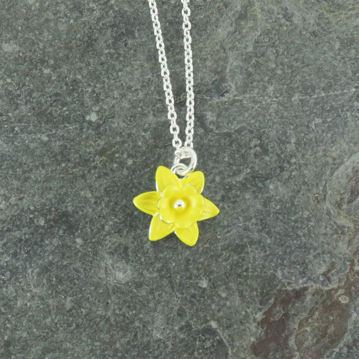 Yellow flower pendant on a silver chain against a gray stone background