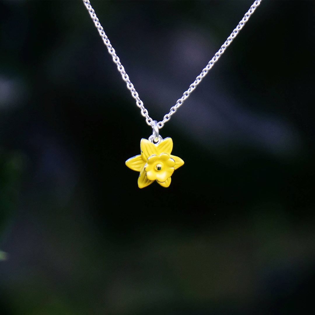 Yellow flower pendant on a silver chain against a dark background