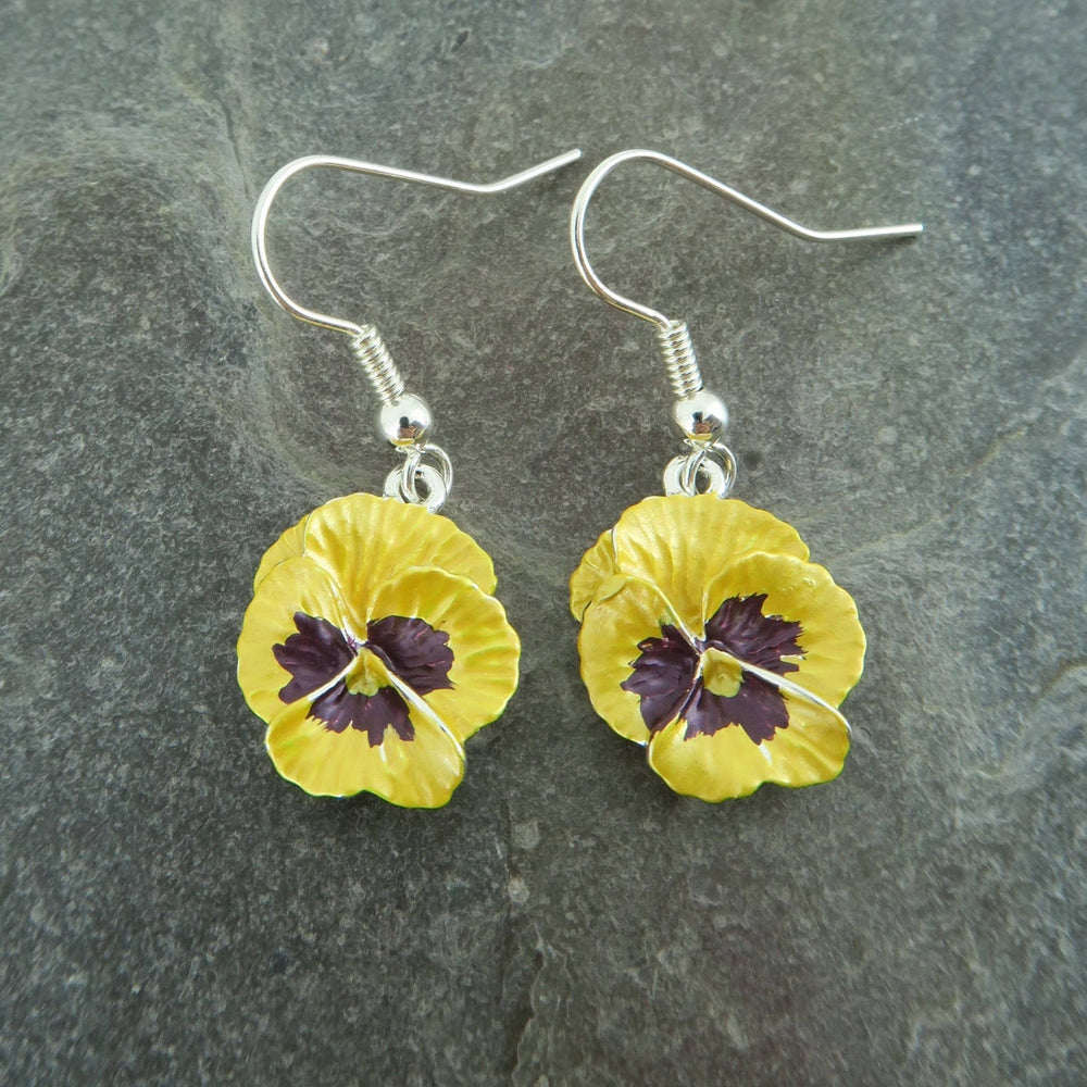 Yellow flower-shaped earrings with purple centers on a gray stone background