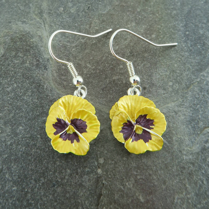 Yellow flower-shaped earrings with purple centers on a gray stone background