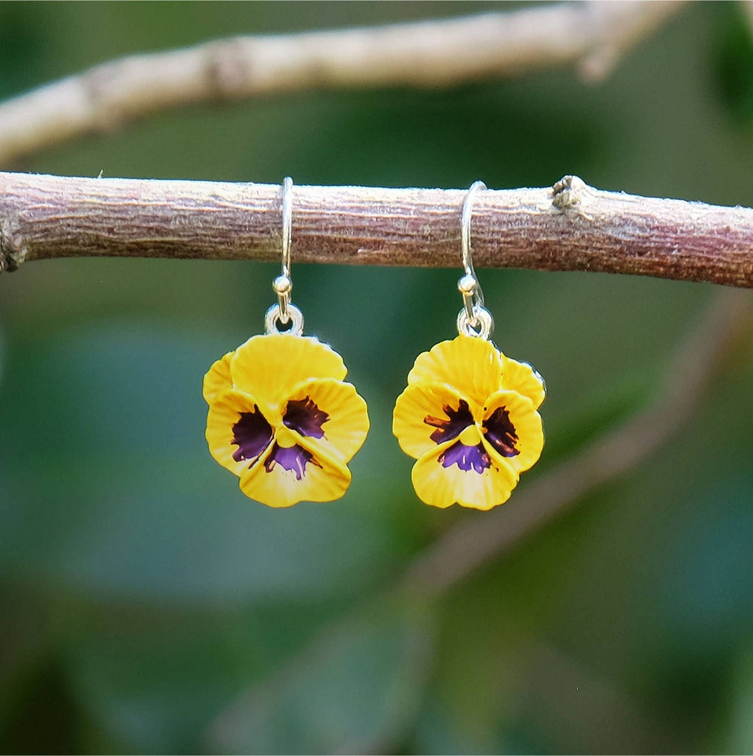 Yellow flower-shaped earrings hanging on a branch with a blurred green background