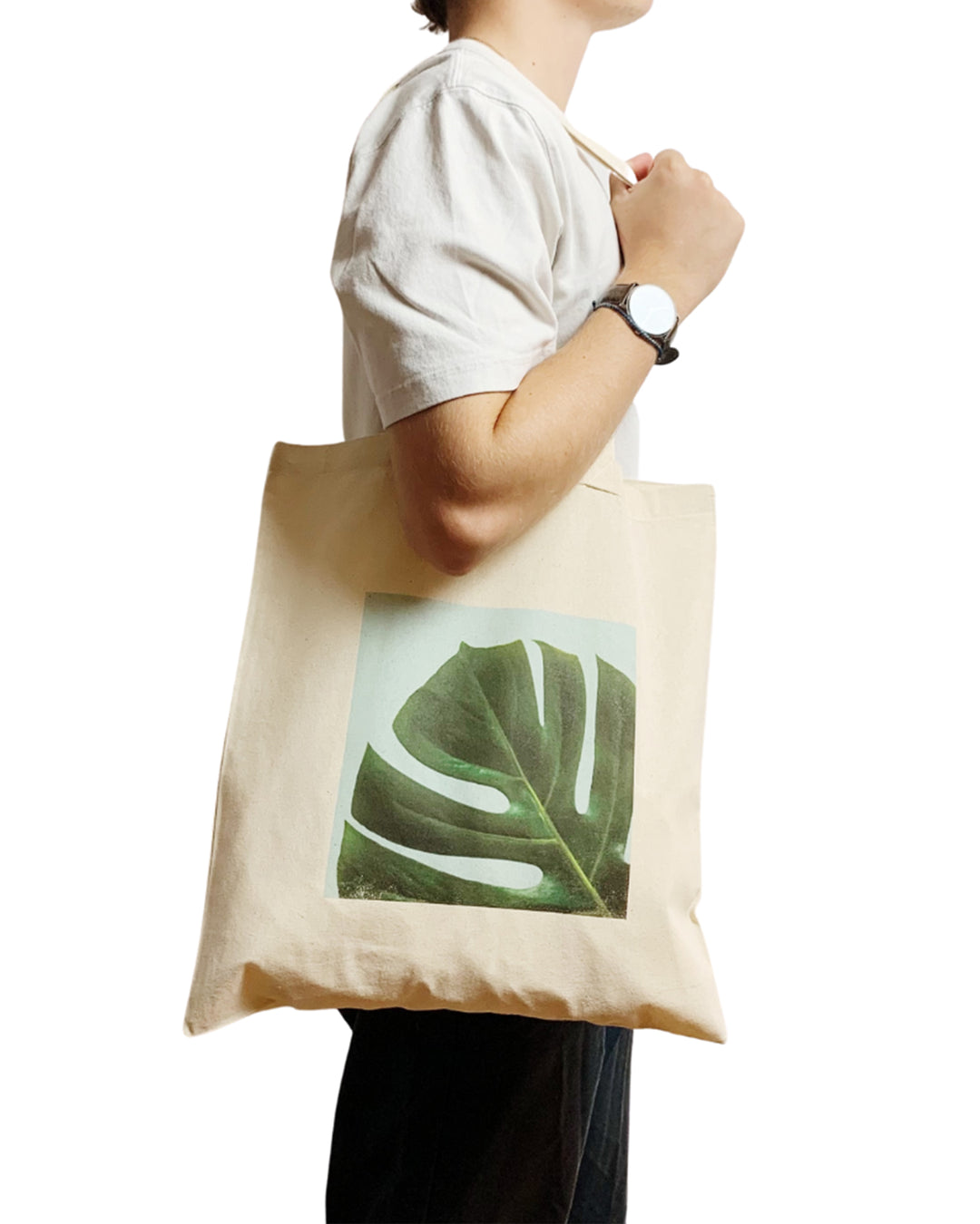 Person holding a beige tote bag with a green leaf design on a white background