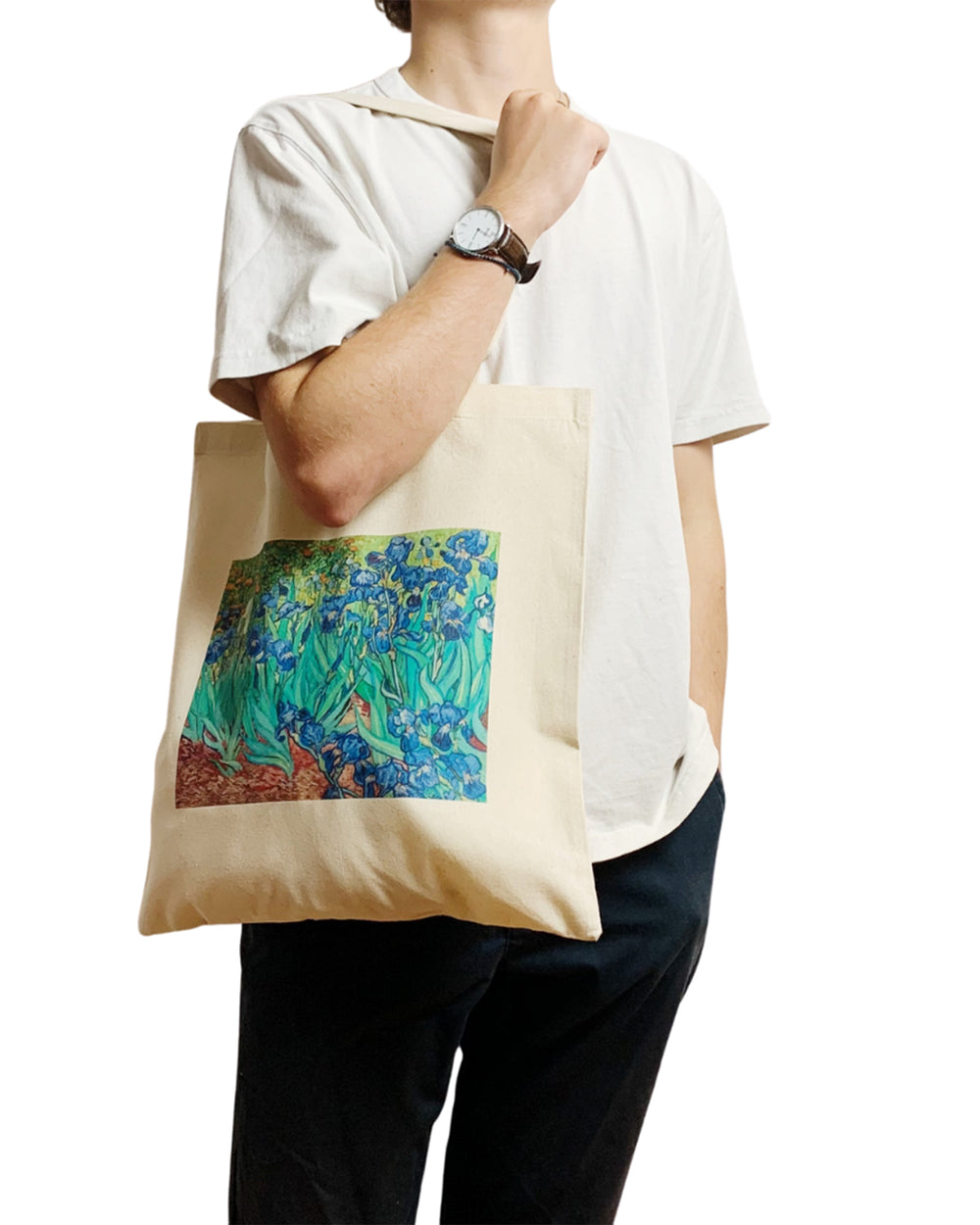 Person holding a tote bag with a colorful design, wearing a white shirt and black pants.